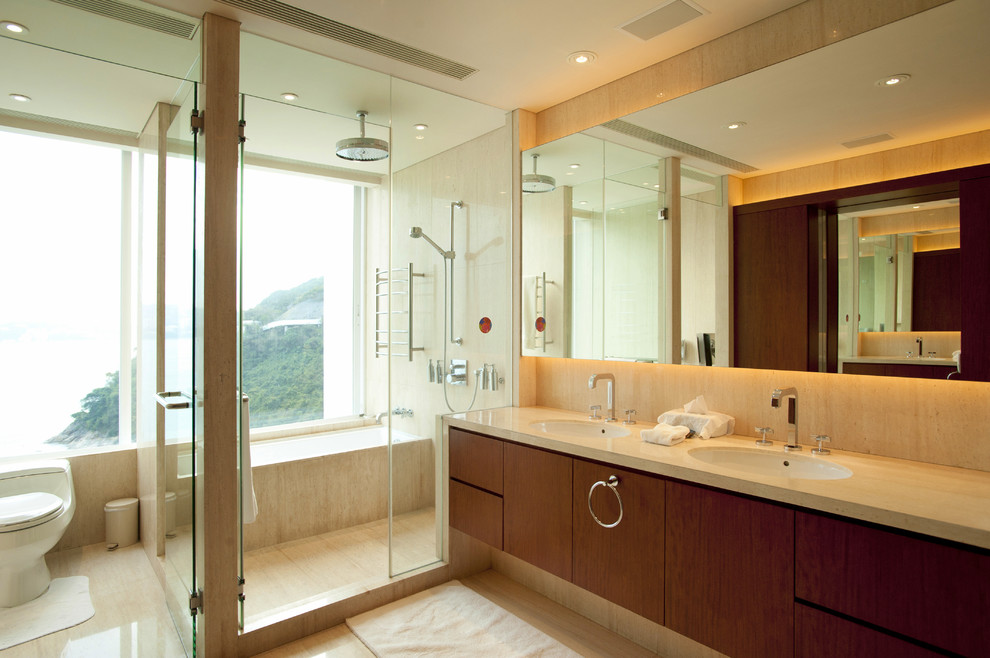Photo of a contemporary master bathroom in Other with furniture-like cabinets, medium wood cabinets, a drop-in tub, a shower/bathtub combo, a one-piece toilet, beige tile, travertine, beige walls, travertine floors, an undermount sink, marble benchtops, beige floor and a hinged shower door.