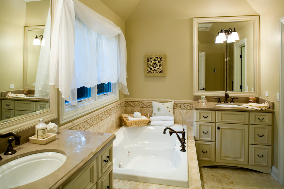 Photo of a mid-sized traditional master bathroom in Chicago with an undermount sink, raised-panel cabinets, distressed cabinets, marble benchtops, a drop-in tub, beige tile, stone tile, beige walls and marble floors.