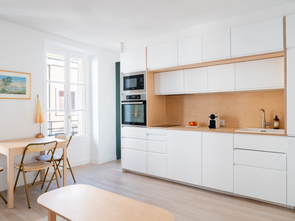 Small scandinavian single-wall open plan kitchen in Paris with a single-bowl sink, wood benchtops, timber splashback, stainless steel appliances and no island.