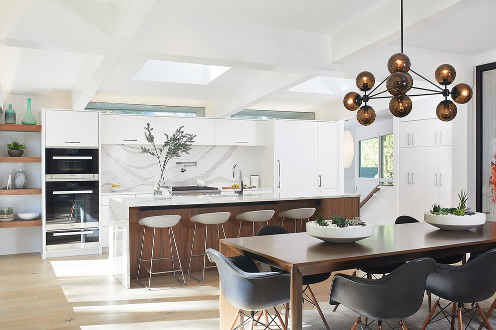 Design ideas for an expansive midcentury galley open plan kitchen in Grand Rapids with an undermount sink, flat-panel cabinets, white cabinets, concrete benchtops, white splashback, stone slab splashback, panelled appliances, light hardwood floors, with island, brown floor and white benchtop.