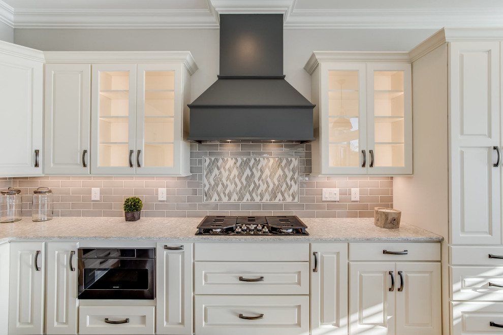 Large transitional l-shaped open concept kitchen photo with an undermount sink, raised-panel cabinets, white cabinets, quartz countertops, gray backsplash, subway tile backsplash, stainless steel appliances, an island and white countertops