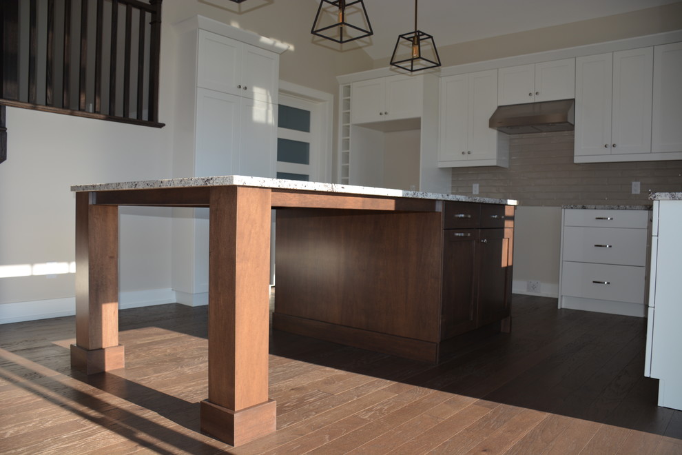Inspiration for a mid-sized transitional u-shaped light wood floor eat-in kitchen remodel in Toronto with a double-bowl sink, shaker cabinets, white cabinets, granite countertops, gray backsplash, subway tile backsplash, stainless steel appliances and an island