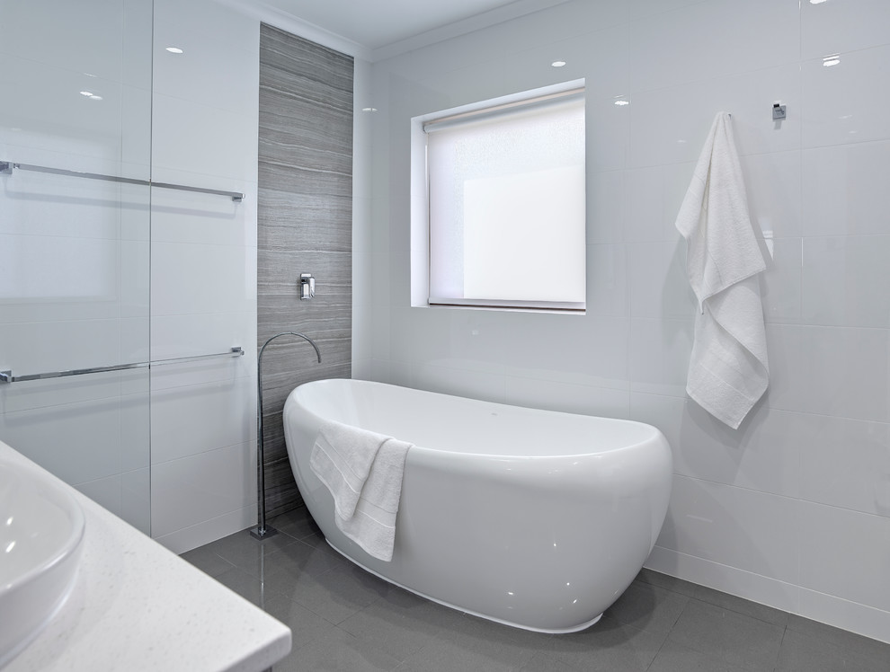Photo of a mid-sized contemporary master bathroom in Other with an integrated sink, light wood cabinets, a freestanding tub, an open shower, a wall-mount toilet, gray tile, white walls and porcelain floors.