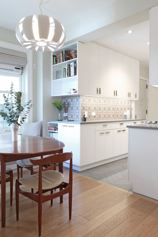 This is an example of a small modern galley eat-in kitchen in New York with a single-bowl sink, flat-panel cabinets, white cabinets, quartz benchtops, multi-coloured splashback, porcelain splashback, stainless steel appliances and porcelain floors.
