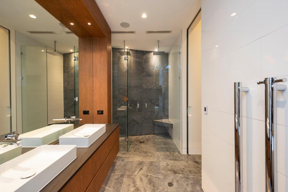 This is an example of a large contemporary master bathroom in Melbourne with flat-panel cabinets, stone tile, a console sink, a hinged shower door, a floating vanity, a double shower, limestone floors, a shower seat and a double vanity.