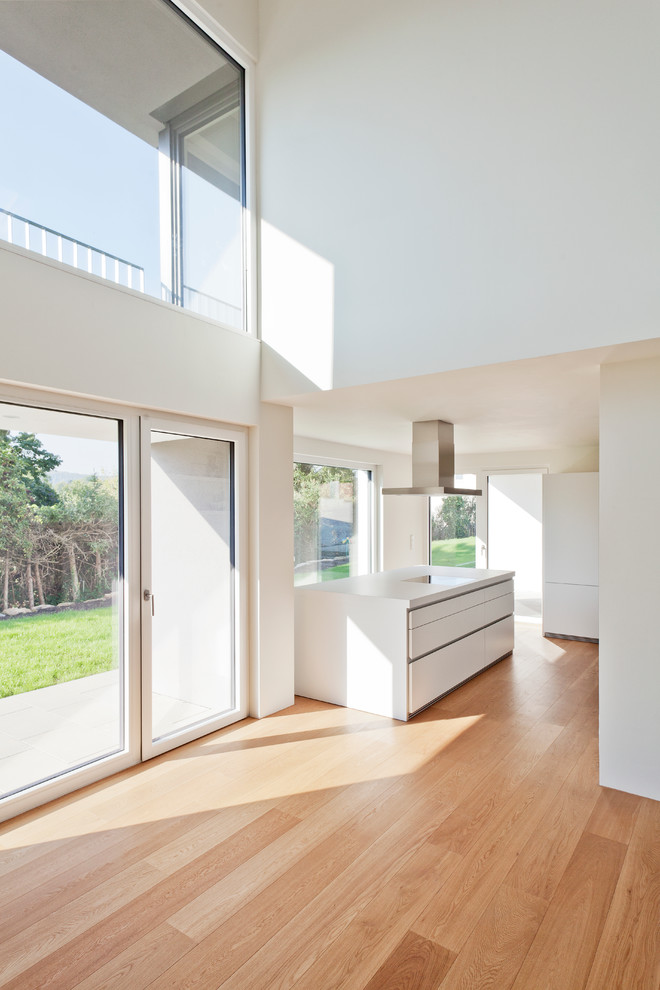 This is an example of a large contemporary open plan kitchen in Stuttgart with flat-panel cabinets, white cabinets, with island and light hardwood floors.