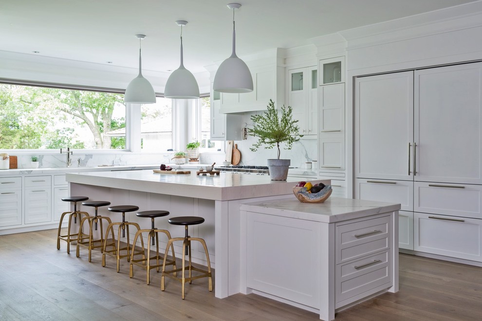 Huge transitional medium tone wood floor and brown floor eat-in kitchen photo with an undermount sink, recessed-panel cabinets, white cabinets, marble countertops, white backsplash, marble backsplash, stainless steel appliances, white countertops and two islands