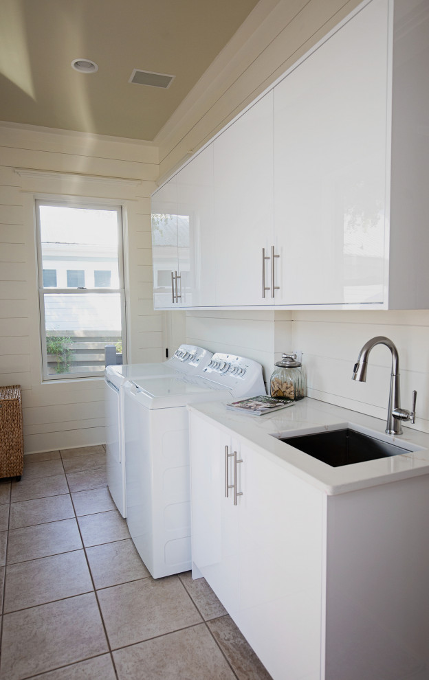 Photo of a mid-sized transitional single-wall utility room in Miami with a drop-in sink, flat-panel cabinets, white cabinets, quartz benchtops, white splashback, shiplap splashback, white walls, ceramic floors, a side-by-side washer and dryer, beige floor, white benchtop and planked wall panelling.