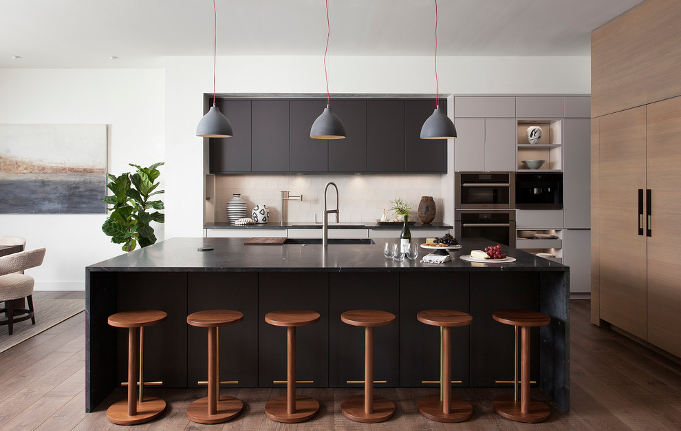 Inspiration for a contemporary l-shaped eat-in kitchen in Austin with an integrated sink, flat-panel cabinets, black cabinets, beige splashback, stainless steel appliances, medium hardwood floors, with island, brown floor and black benchtop.