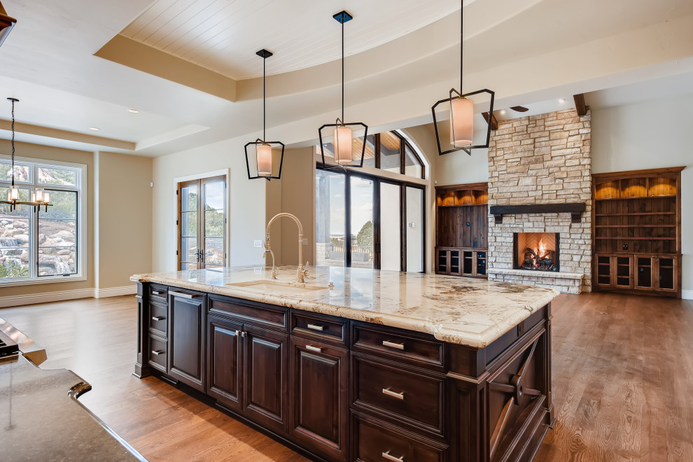 Photo of an expansive traditional l-shaped open plan kitchen in Denver with raised-panel cabinets, brown cabinets, granite benchtops, beige splashback, panelled appliances, medium hardwood floors, with island, brown floor and brown benchtop.