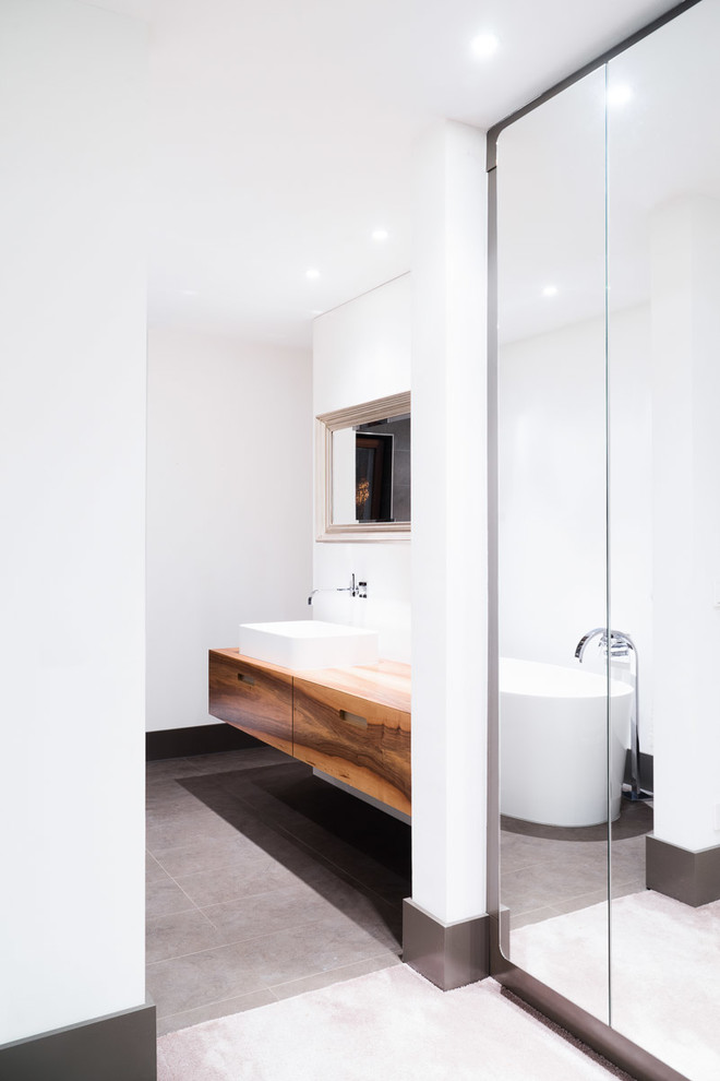 Photo of a mid-sized contemporary master bathroom in Stuttgart with flat-panel cabinets, medium wood cabinets, a freestanding tub, gray tile, white walls, a vessel sink and wood benchtops.