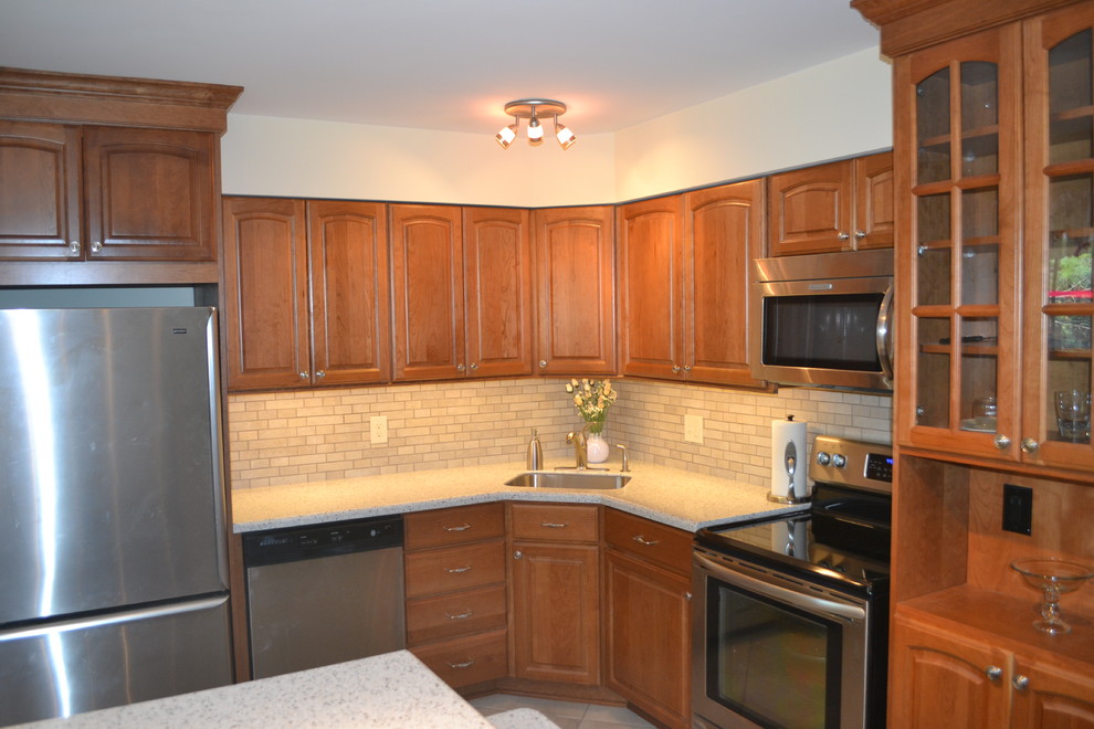 Photo of a small classic l-shaped kitchen/diner in Philadelphia with a submerged sink, raised-panel cabinets, medium wood cabinets, composite countertops, beige splashback, metro tiled splashback, stainless steel appliances, porcelain flooring and an island.