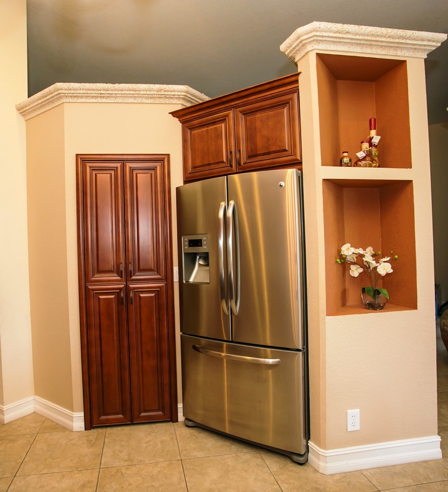 Eat-in kitchen - mid-sized transitional u-shaped porcelain tile eat-in kitchen idea in Miami with an undermount sink, raised-panel cabinets, brown cabinets, granite countertops, beige backsplash, stone tile backsplash, stainless steel appliances, beige walls and a peninsula