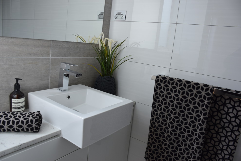 Small contemporary master bathroom in Melbourne with white cabinets, engineered quartz benchtops, a corner shower, a two-piece toilet, gray tile, cement tile, white walls and ceramic floors.