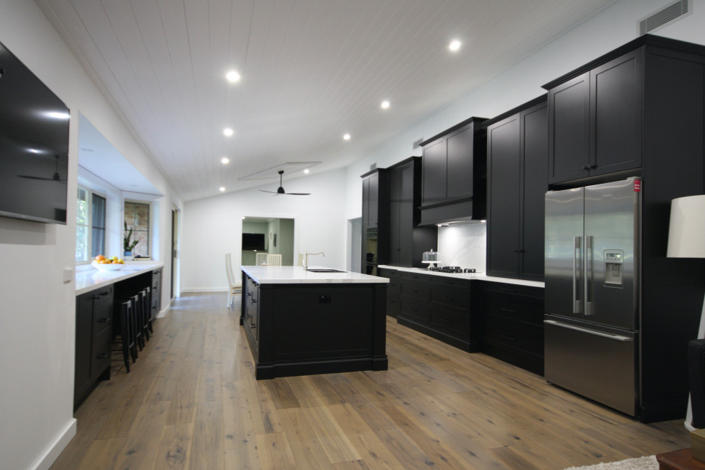 Exempel på ett mycket stort klassiskt vit vitt kök, med en undermonterad diskho, skåp i shakerstil, svarta skåp, bänkskiva i kvarts, vitt stänkskydd, rostfria vitvaror, mellanmörkt trägolv, en köksö och brunt golv