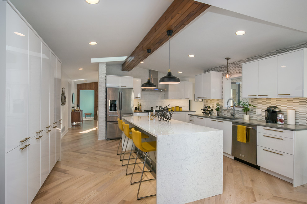 Midcentury l-shaped kitchen in Grand Rapids with an undermount sink, flat-panel cabinets, white cabinets, grey splashback, stainless steel appliances, light hardwood floors, with island and beige floor.