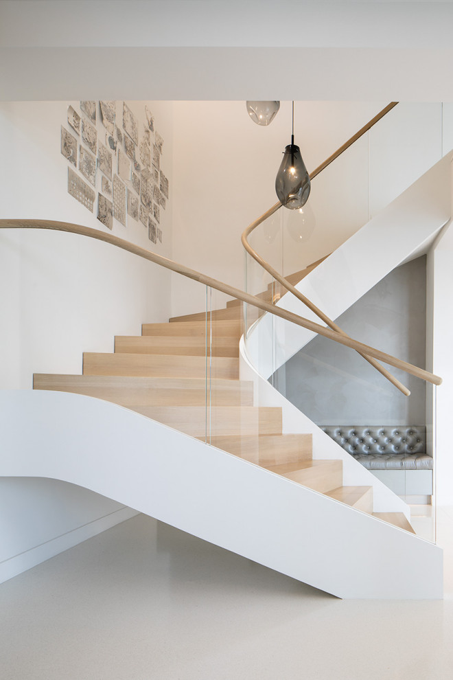 Diseño de escalera curva minimalista con escalones de madera, contrahuellas de madera y barandilla de vidrio