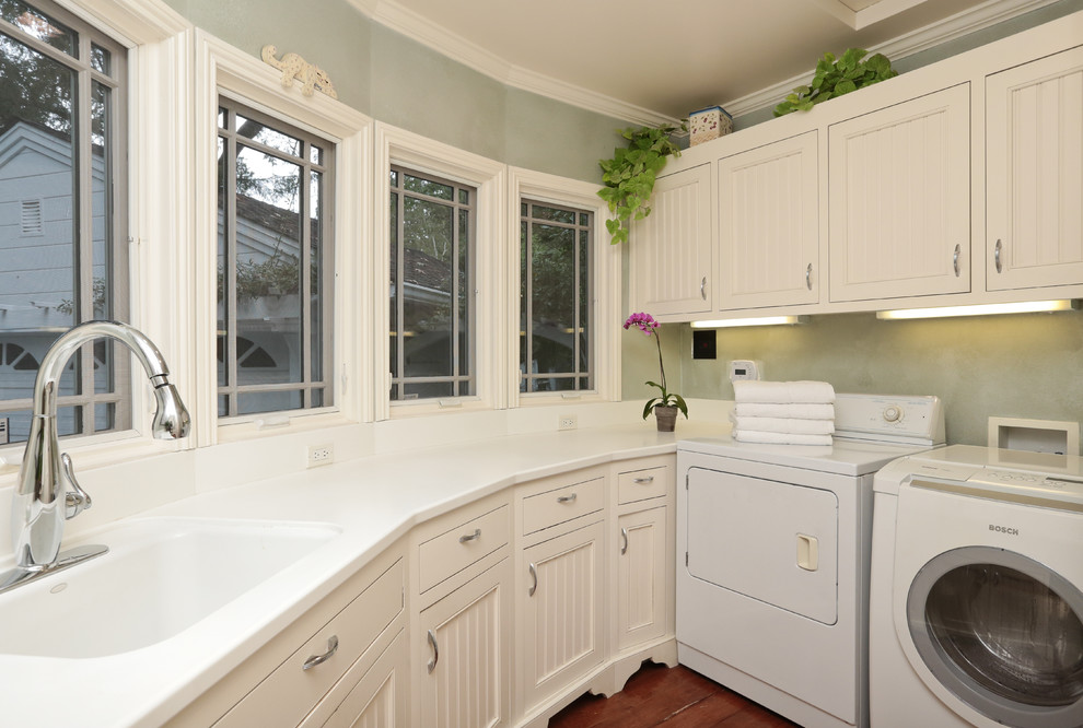 Design ideas for a mid-sized traditional u-shaped dedicated laundry room in San Francisco with an undermount sink, beaded inset cabinets, white cabinets, solid surface benchtops, blue walls, dark hardwood floors and a side-by-side washer and dryer.