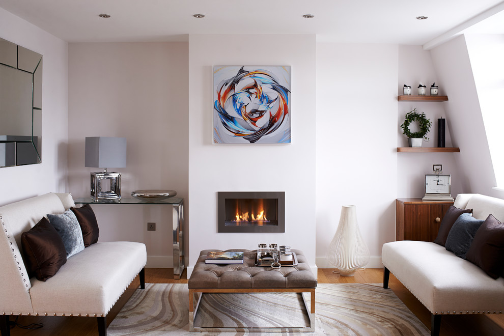 This is an example of a small contemporary formal living room in London with white walls, medium hardwood floors, a standard fireplace, a metal fireplace surround and no tv.