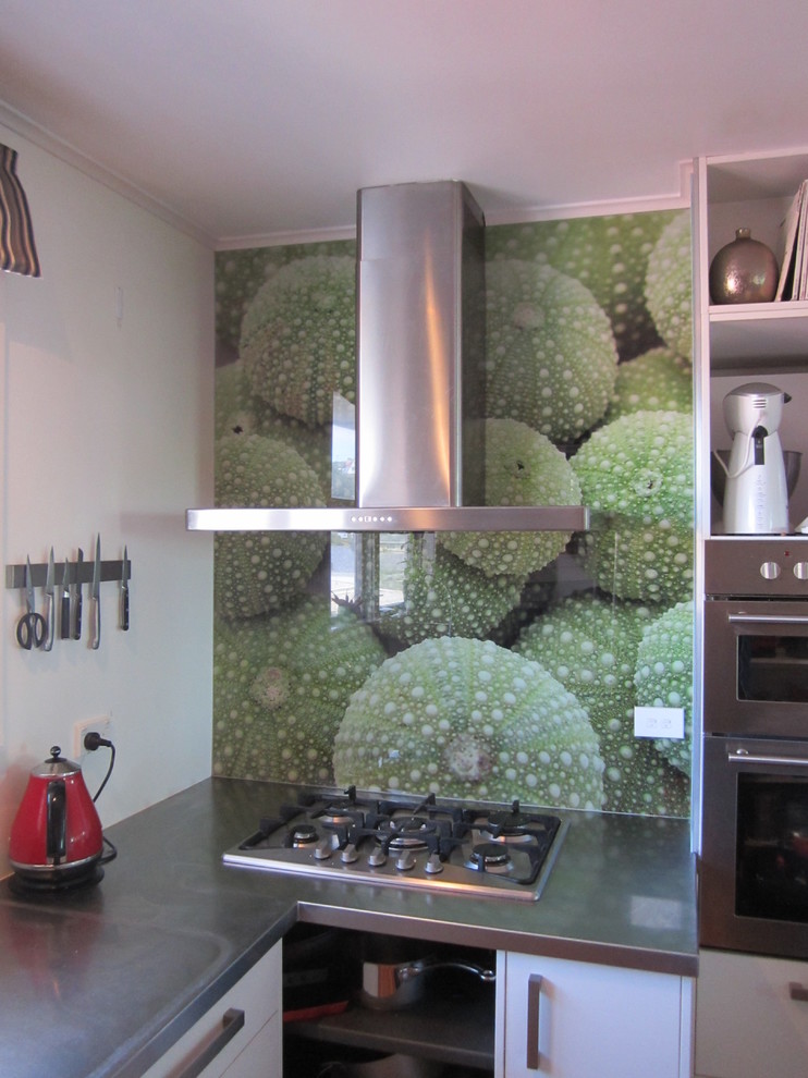 Cette image montre une petite cuisine minimaliste en L avec un plan de travail en inox, une crédence multicolore et une crédence en feuille de verre.