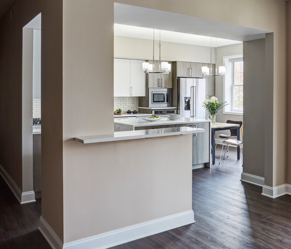 This is an example of a large contemporary l-shaped eat-in kitchen in Chicago with an undermount sink, flat-panel cabinets, grey cabinets, quartz benchtops, white splashback, subway tile splashback, stainless steel appliances, porcelain floors, with island, grey floor and white benchtop.