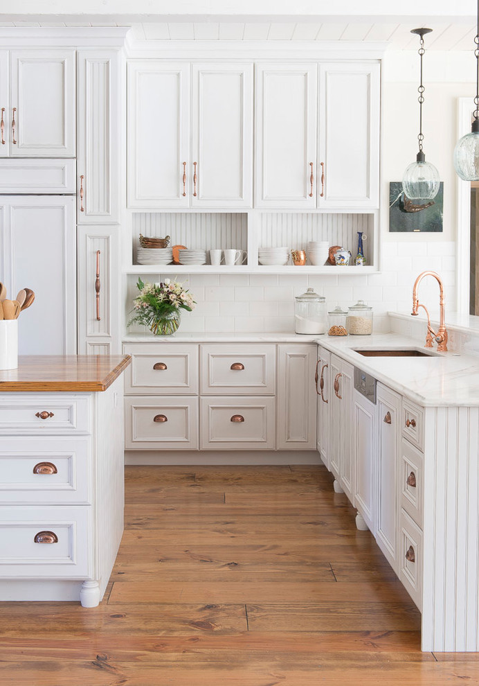 Inspiration for a large l-shaped open plan kitchen in St Louis with an undermount sink, recessed-panel cabinets, white cabinets, quartzite benchtops, white splashback, subway tile splashback, panelled appliances, light hardwood floors and with island.