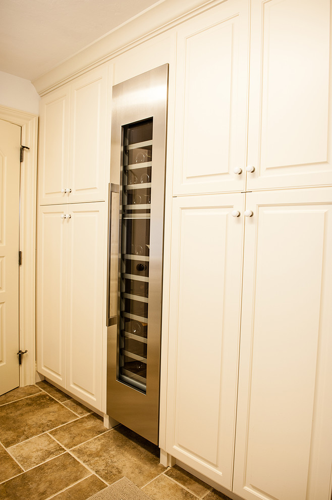 This is an example of a mid-sized traditional galley utility room in Miami with a single-bowl sink, raised-panel cabinets, white cabinets, white walls, travertine floors, a side-by-side washer and dryer and beige floor.