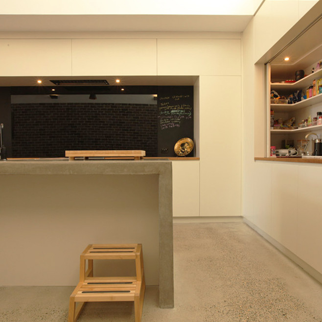 Photo of a large contemporary galley kitchen pantry in Sydney with a double-bowl sink, white cabinets, concrete benchtops, black splashback, glass sheet splashback, panelled appliances, concrete floors and with island.