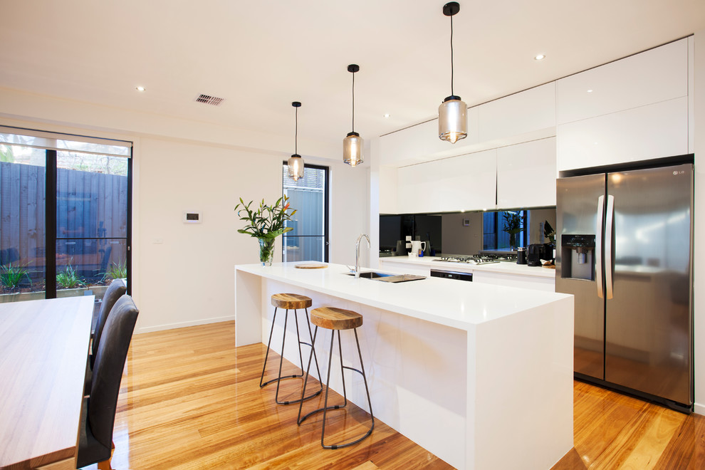 Inspiration for a contemporary galley eat-in kitchen in Melbourne with an undermount sink, flat-panel cabinets, white cabinets, solid surface benchtops, black splashback, stainless steel appliances, medium hardwood floors and with island.