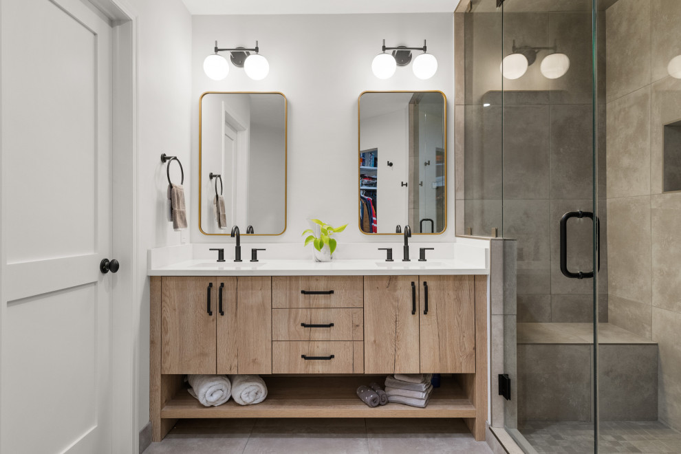 Photo of a mid-sized transitional master bathroom in Calgary with flat-panel cabinets, light wood cabinets, an alcove shower, gray tile, ceramic tile, ceramic floors, an undermount sink, engineered quartz benchtops, a hinged shower door, white benchtops, a niche, a double vanity and a freestanding vanity.