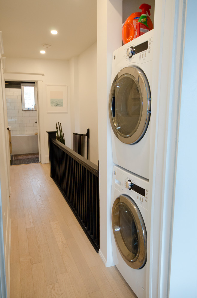Small contemporary single-wall laundry cupboard in Toronto with white walls, medium hardwood floors, a stacked washer and dryer and beige floor.