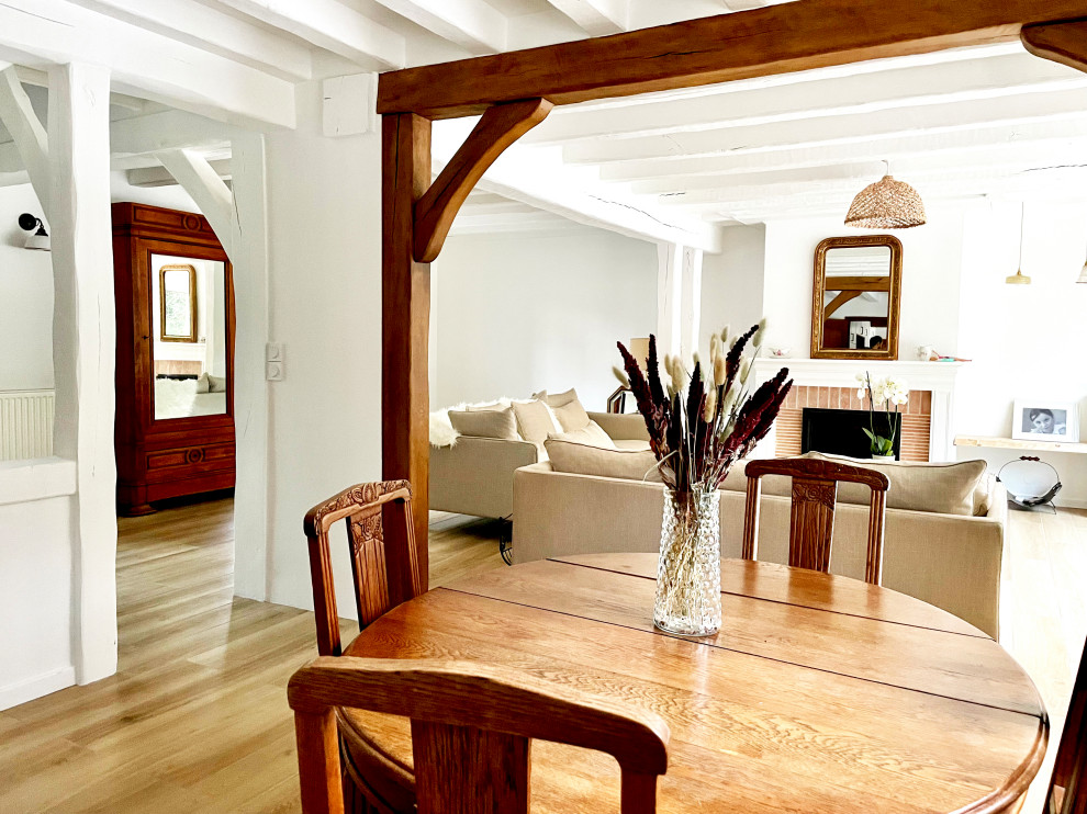 Immagine di una grande sala da pranzo aperta verso il soggiorno country con pareti bianche, travi a vista, parquet chiaro, stufa a legna e pavimento beige