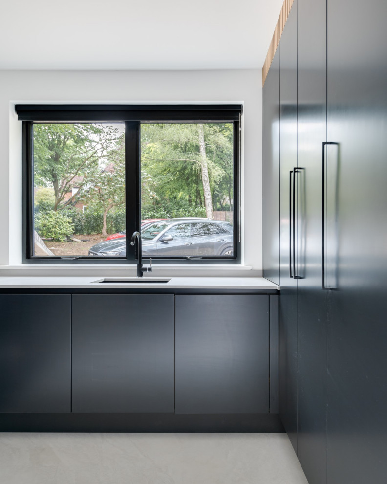 Inspiration for an expansive modern l-shaped utility room in Hertfordshire with an integrated sink, flat-panel cabinets, black cabinets, quartzite benchtops, white walls, porcelain floors, a concealed washer and dryer, grey floor and grey benchtop.