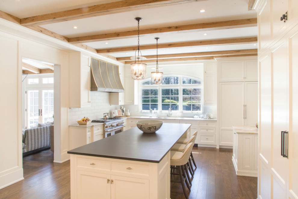 Large transitional l-shaped painted wood floor, brown floor and exposed beam eat-in kitchen photo in New York with shaker cabinets, white cabinets, quartz countertops, white backsplash, quartz backsplash, two islands and black countertops