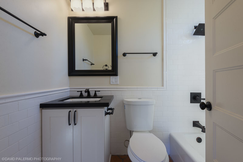 Photo of a small mediterranean bathroom in Santa Barbara with an undermount sink, shaker cabinets, white cabinets, granite benchtops, an alcove tub, a shower/bathtub combo, a two-piece toilet, white tile, ceramic tile, white walls and terra-cotta floors.