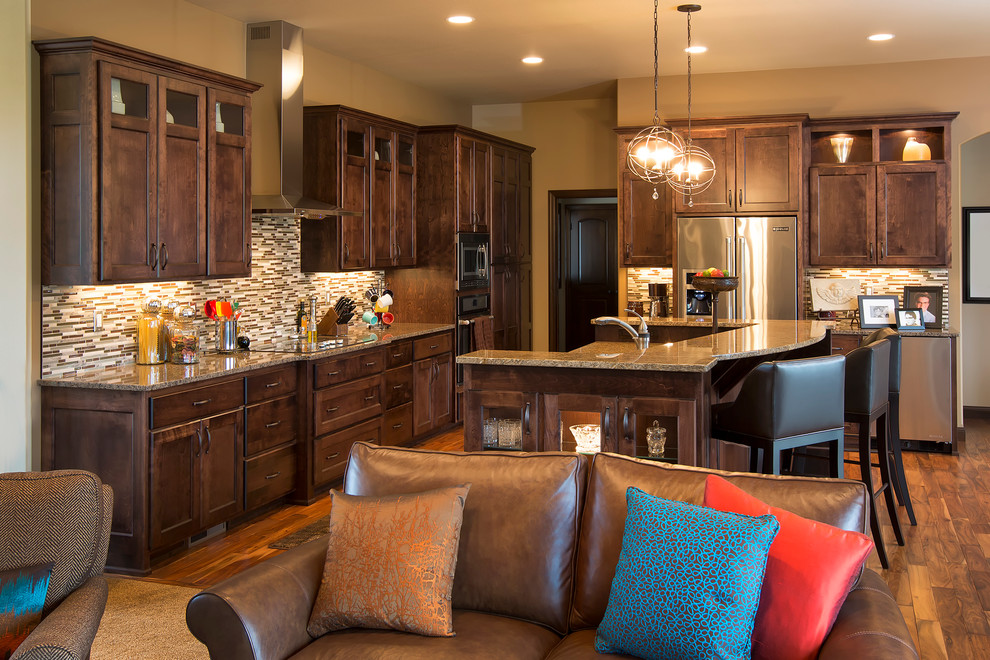 Transitional l-shaped medium tone wood floor open concept kitchen photo with an undermount sink, recessed-panel cabinets, dark wood cabinets, granite countertops, multicolored backsplash, mosaic tile backsplash, stainless steel appliances and an island