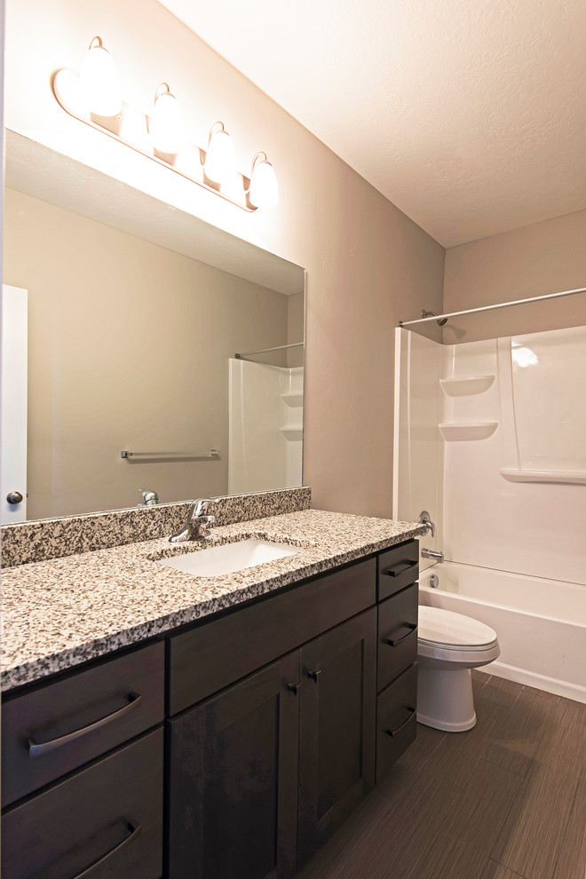 Inspiration for a mid-sized arts and crafts 3/4 bathroom in Salt Lake City with shaker cabinets, dark wood cabinets, an alcove tub, a shower/bathtub combo, a one-piece toilet, laminate floors, an undermount sink, granite benchtops and brown floor.