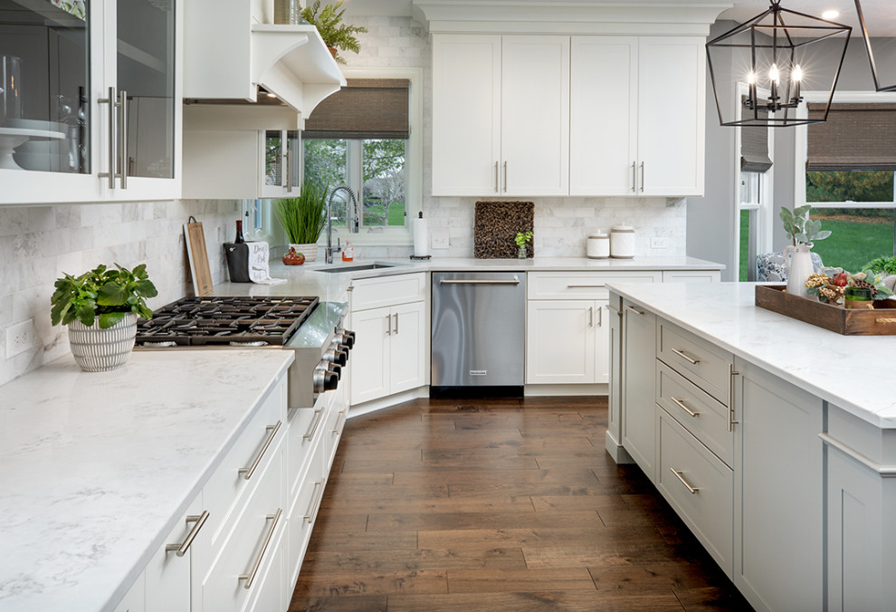 This is an example of a large transitional l-shaped eat-in kitchen in Columbus with an undermount sink, shaker cabinets, white cabinets, quartz benchtops, white splashback, marble splashback, stainless steel appliances, medium hardwood floors, with island, brown floor and white benchtop.