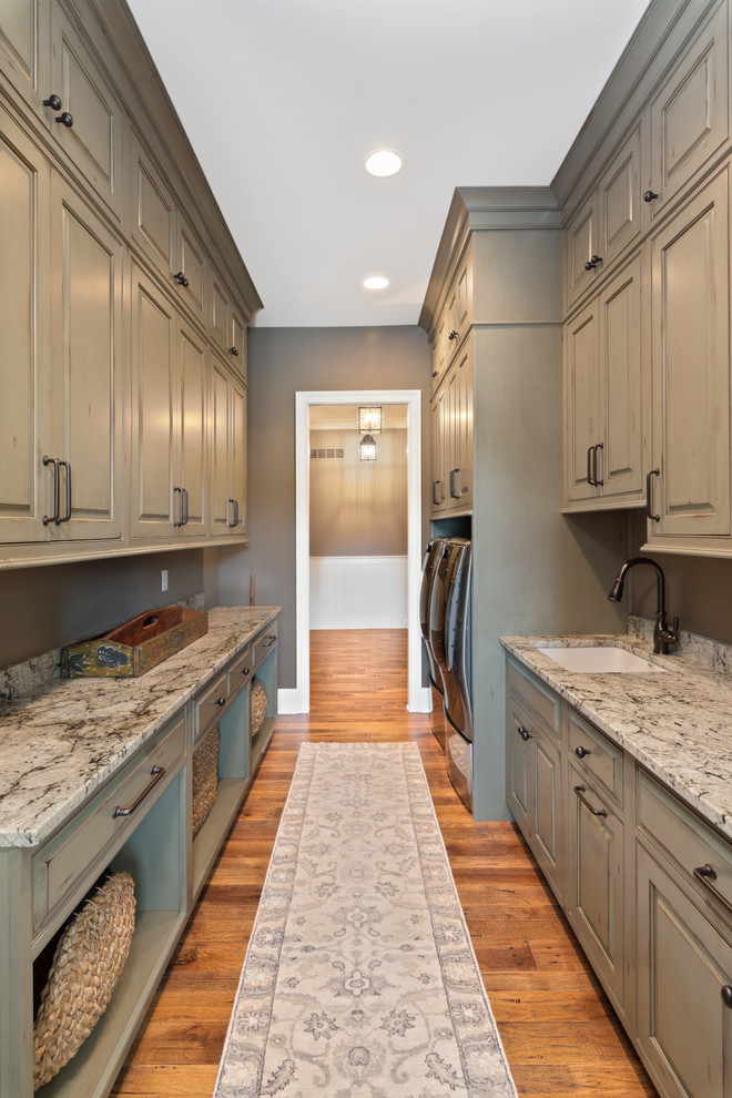 Inspiration for a large traditional galley dedicated laundry room in Cincinnati with an undermount sink, raised-panel cabinets, grey cabinets, granite benchtops, grey walls, dark hardwood floors, a side-by-side washer and dryer, brown floor and grey benchtop.