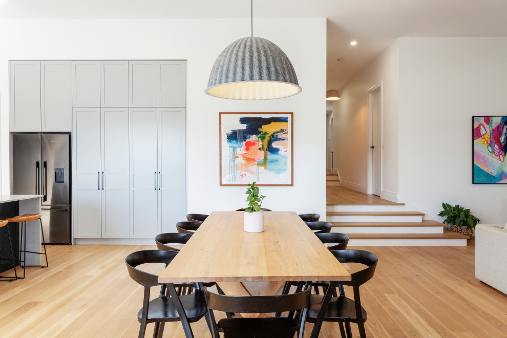 Cette image montre une grande salle à manger ouverte sur le salon design avec un mur blanc, parquet clair et un sol beige.