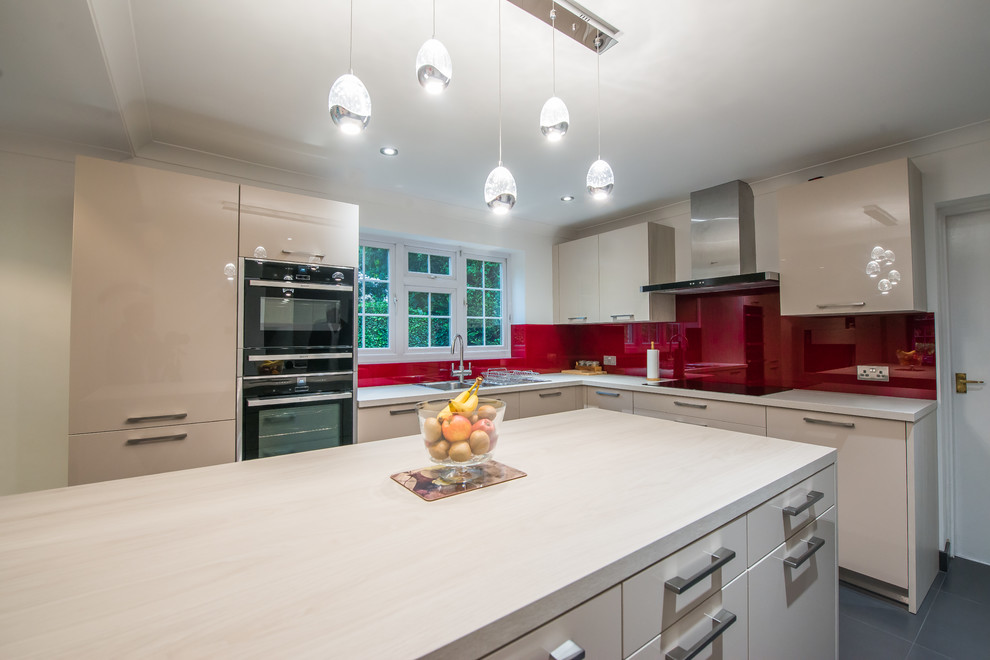 Design ideas for a contemporary l-shaped kitchen in London with a double-bowl sink, flat-panel cabinets, light wood cabinets, onyx benchtops, red splashback, glass sheet splashback, black appliances and with island.