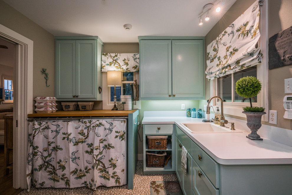 Inspiration for a mid-sized country l-shaped dedicated laundry room in Austin with a drop-in sink, recessed-panel cabinets, a concealed washer and dryer, white benchtop, blue cabinets and grey walls.