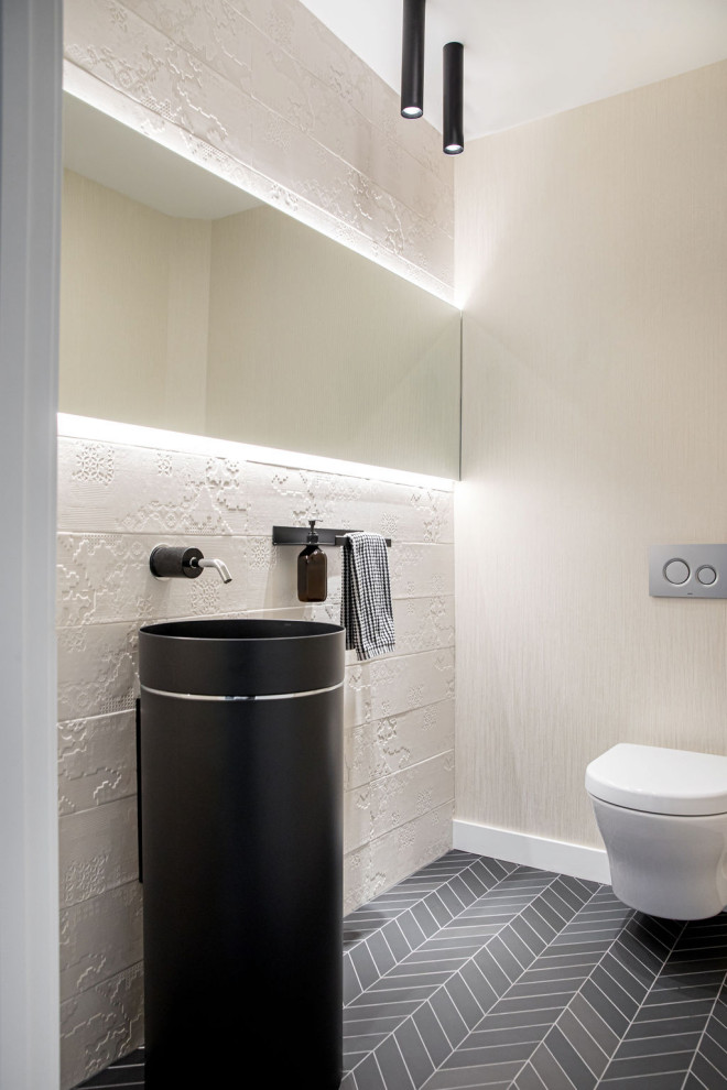 Small modern cloakroom in Calgary with a wall mounted toilet, white tiles, porcelain tiles, white walls, porcelain flooring, a pedestal sink, black floors and wallpapered walls.