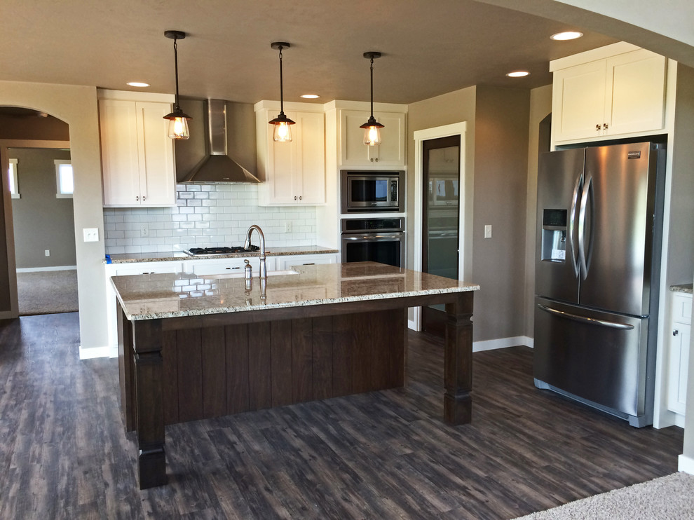 Large arts and crafts open plan kitchen in Milwaukee with a farmhouse sink, shaker cabinets, white cabinets, granite benchtops, white splashback, subway tile splashback, stainless steel appliances, vinyl floors and with island.