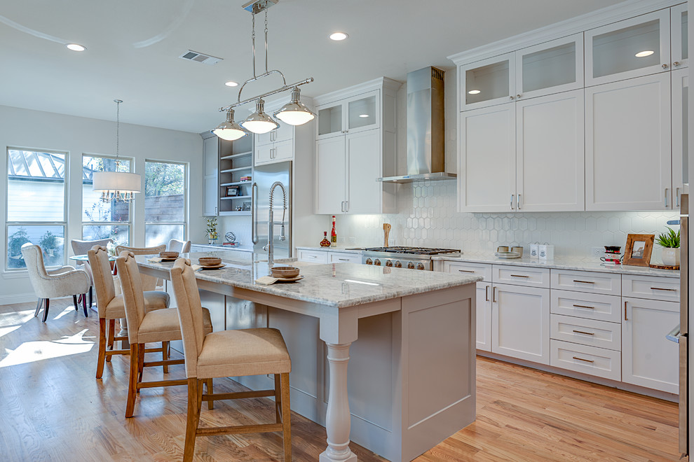 Mid-sized transitional galley open plan kitchen in Dallas with shaker cabinets, white cabinets, white splashback, stainless steel appliances, light hardwood floors, with island, a farmhouse sink, granite benchtops, ceramic splashback and beige floor.