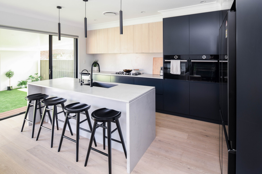 This is an example of a large modern l-shaped kitchen in Sydney with an undermount sink, flat-panel cabinets, blue cabinets, quartz benchtops, white splashback, engineered quartz splashback, black appliances, light hardwood floors, with island, white benchtop and beige floor.