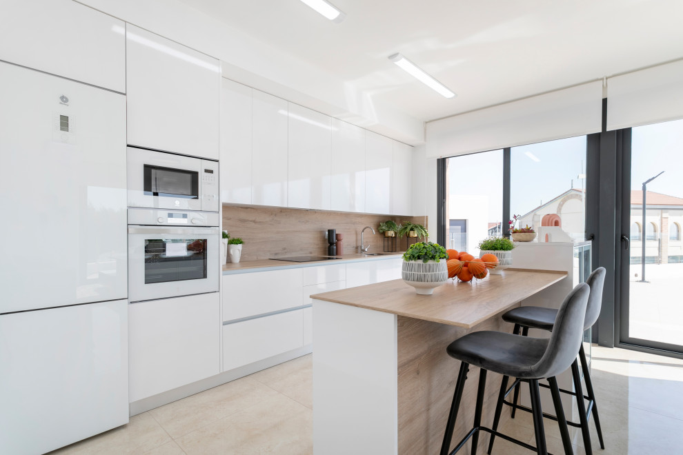 Photo of a contemporary galley kitchen in Alicante-Costa Blanca with flat-panel cabinets, white cabinets, wood benchtops, beige splashback, timber splashback, white appliances, a peninsula, beige floor and beige benchtop.