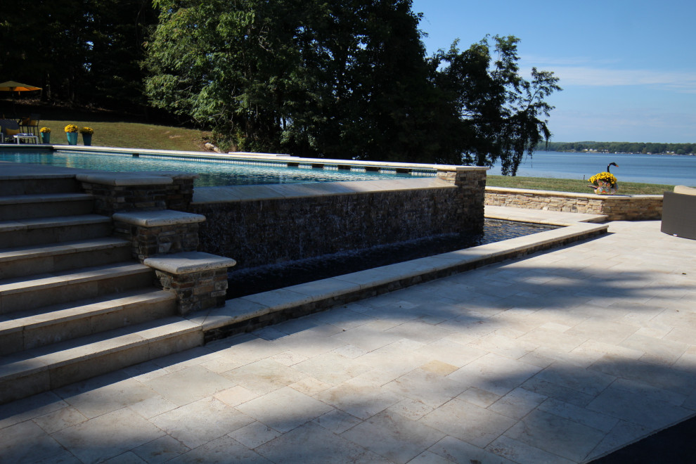 Photo of a large traditional backyard rectangular infinity pool in DC Metro with a hot tub and natural stone pavers.