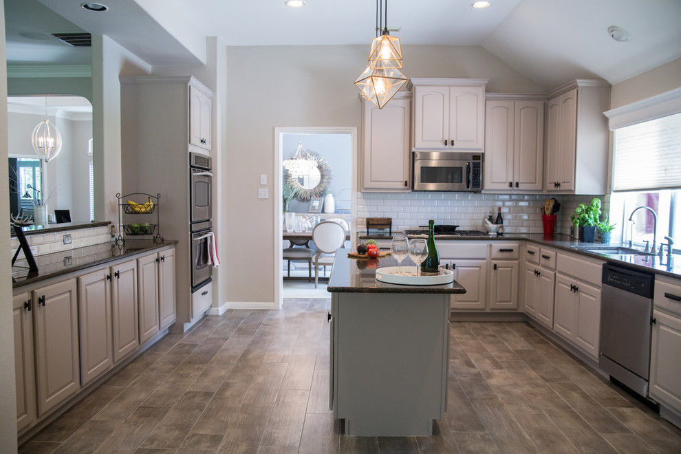 Kitchen - transitional u-shaped porcelain tile and brown floor kitchen idea in Austin with beige cabinets, granite countertops, white backsplash, subway tile backsplash, stainless steel appliances and an island