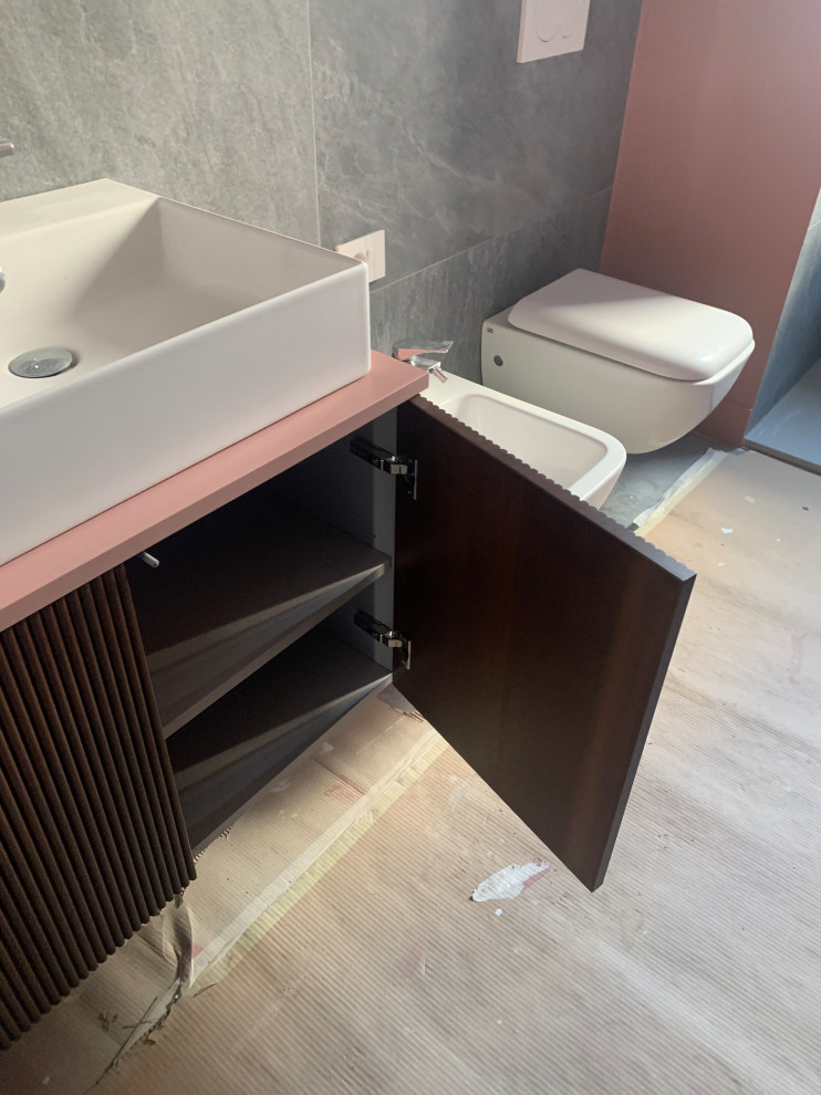 Inspiration for a small contemporary 3/4 bathroom in Milan with louvered cabinets, dark wood cabinets, a curbless shower, a wall-mount toilet, gray tile, porcelain tile, pink walls, porcelain floors, a vessel sink, laminate benchtops, grey floor, a hinged shower door, pink benchtops, a single vanity and a floating vanity.